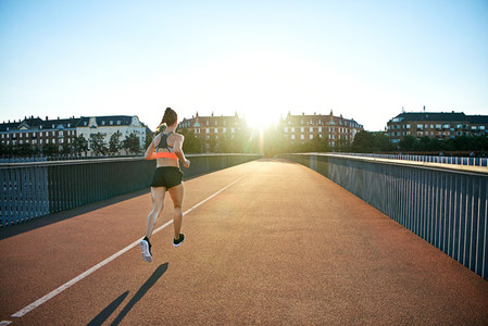 Rear view of athlete jogging toward bright sun