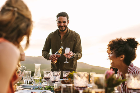 Smiling man serving champagne to friends at party