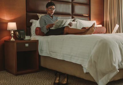 Mature businesswoman relaxing on hotel room bed with newspaper