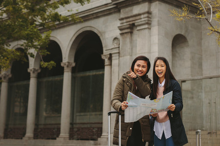 Two female tourists standing on street holding a city map
