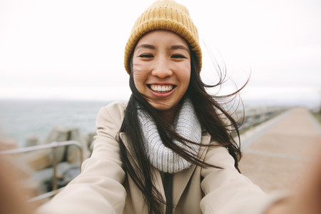 Close up of a smiling woman in winter wear standing near the sea