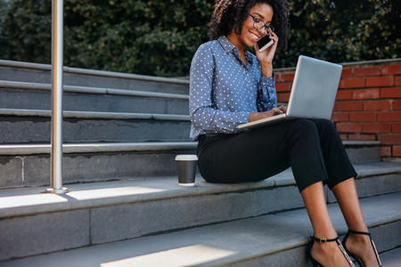 Businesswoman on steps with phone and laptop