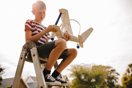 Boy siting on ladder with toy airplane
