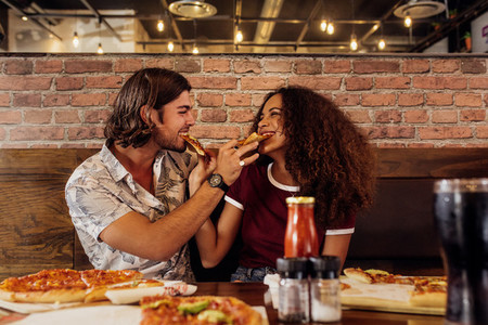 Loving couple feeding each other pizza
