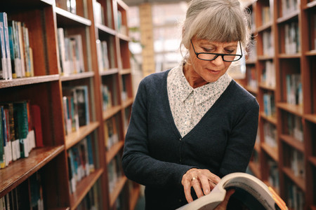 Senior woman looking at a book standing in library