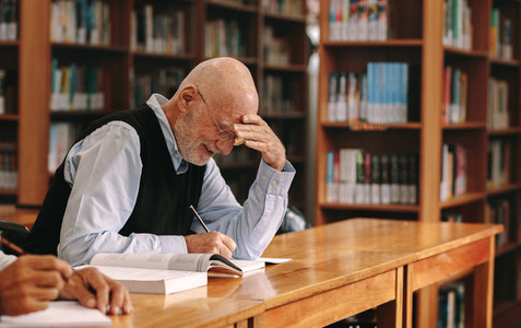 Senior man writing in a book sitting in classroom