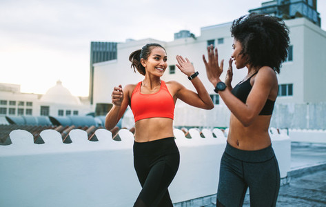 Women athletes giving high five while running on rooftop