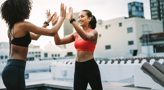 Smiling fitness women giving high five standing on rooftop