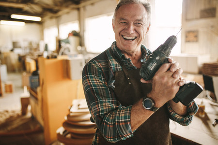 Smiling senior carpenter holding drill machine