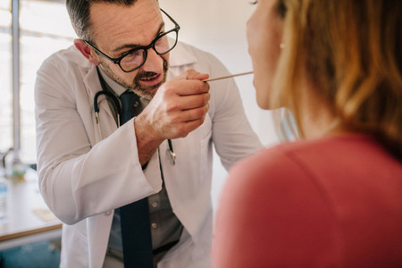 Doctor checking woman throat with the medical stick