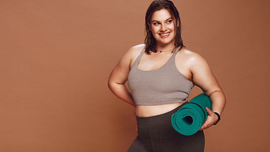Smiling oversized woman with yoga mat