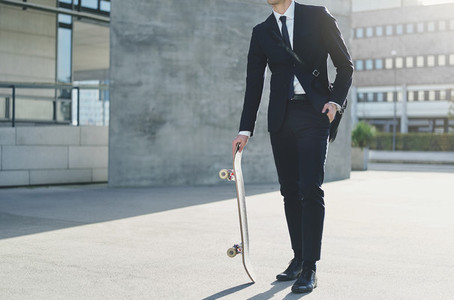 Man wearing suit standing and holding skateboard