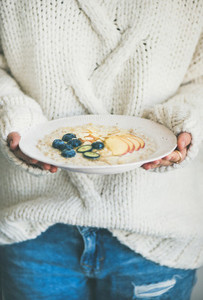 Woman in jeans and sweater holding plate of oatmeal porriage