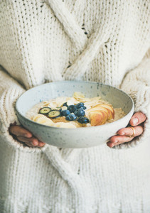 Woman in sweater holding bowl of oatmeal porriage
