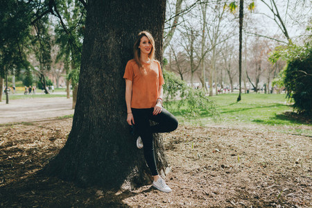 Young smiling blonde woman supported on a tree with black jeans