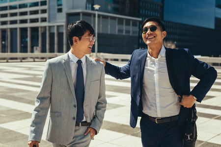 Two smiling businessmen talking and walking in the city