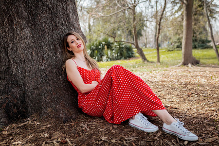 Young smile blond woman sitting near tree with red long dress