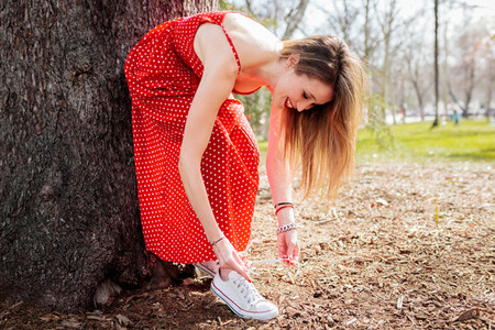 Young smiling blond woman leaning tying her sneakers whit dress