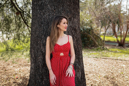 Young smiling blond woman with red dress leaning against a tree