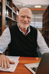 Cheerful senior man learning sitting at a library
