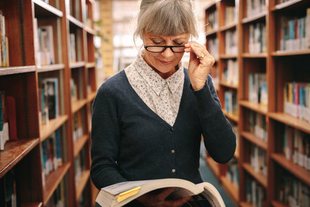 Portrait of a senior woman in eyeglasses reading a book in libra