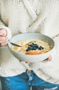 Woman in jeans and sweater eating oatmeal porriage