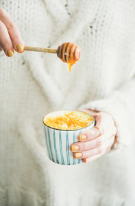 Turmeric latte or golden milk with honey in womans hands