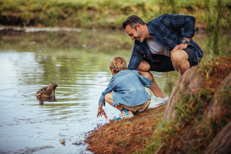 Father teaching little son fishing at pond