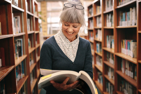 Smiling senior woman looking at a book standing in a library