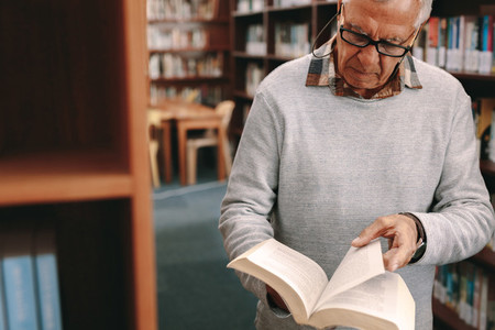 Portrait of a senior man looking at a book in library