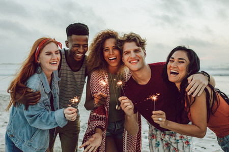 Multiracial friends enjoying at beach with sparklers