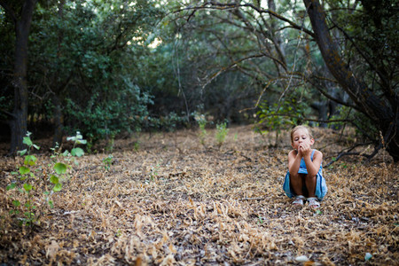 Lonely sad little girl squatting in the forest