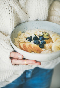Woman in jeans and sweater holding bowl of oatmeal porriage