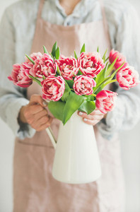 Woman holding white enamel vase with fresh pink tulips