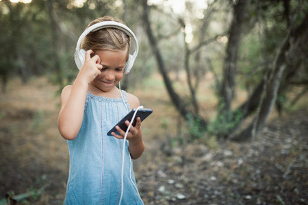 Little girl listening music with her headphones in the forest