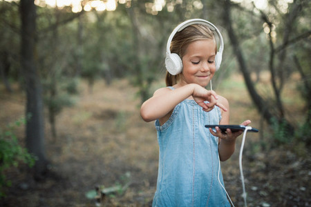 Little girl listening music with her headphones in the forest