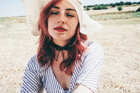 Redhead model protecting herself from sun with a hat in summer