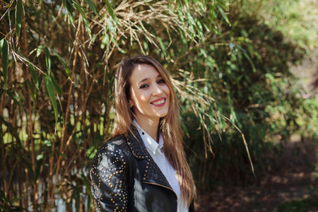 Young smiling blonde woman wearing a leather jacket in the park