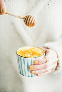 Turmeric latte  golden milk with honey in womans hands  close up