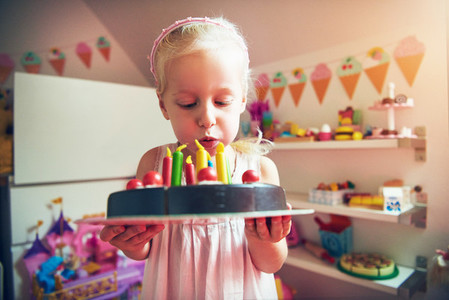 Little girl blows on toy cake candles
