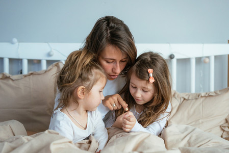 Mom and two daughters draw in bed