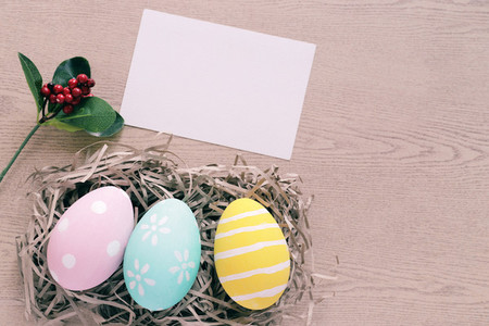 Pastel and colorful easter eggs in nest with blank card on woode