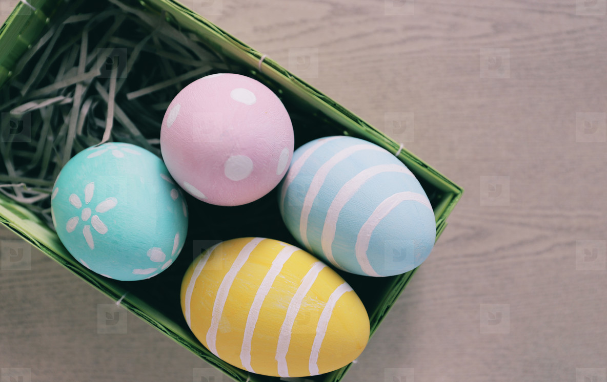Pastel and colorful easter eggs in nest and basket on wooden bac