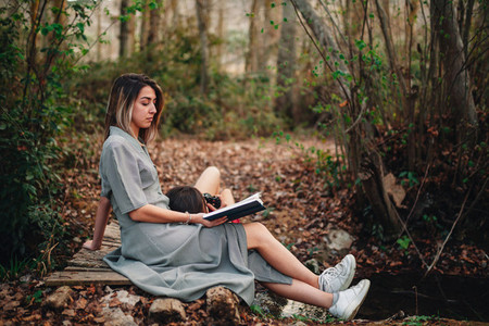 Young women reading a book and taking photos in the forest