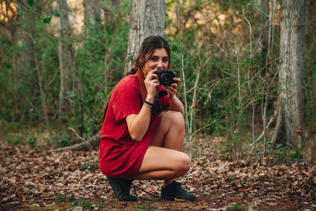 Young smiling woman taking photos in the forest wearing a dress