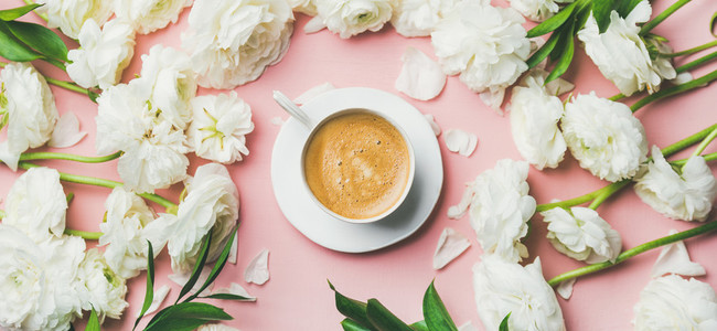 Cup of coffee and white ranunculus flowers on pink background