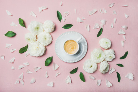 Cup of coffee surrounded with white ranunculus flowers and petals