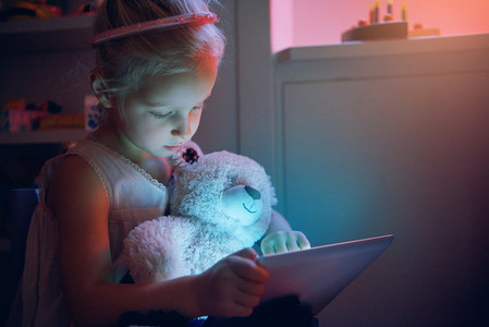 Little child browsing tablet with toy bear