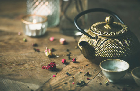 Golden iron teapot  cups  dried rose  candles over wooden background