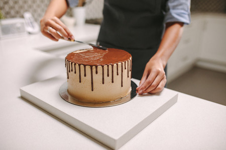 Confectioner decorates a cake with liquid chocolate